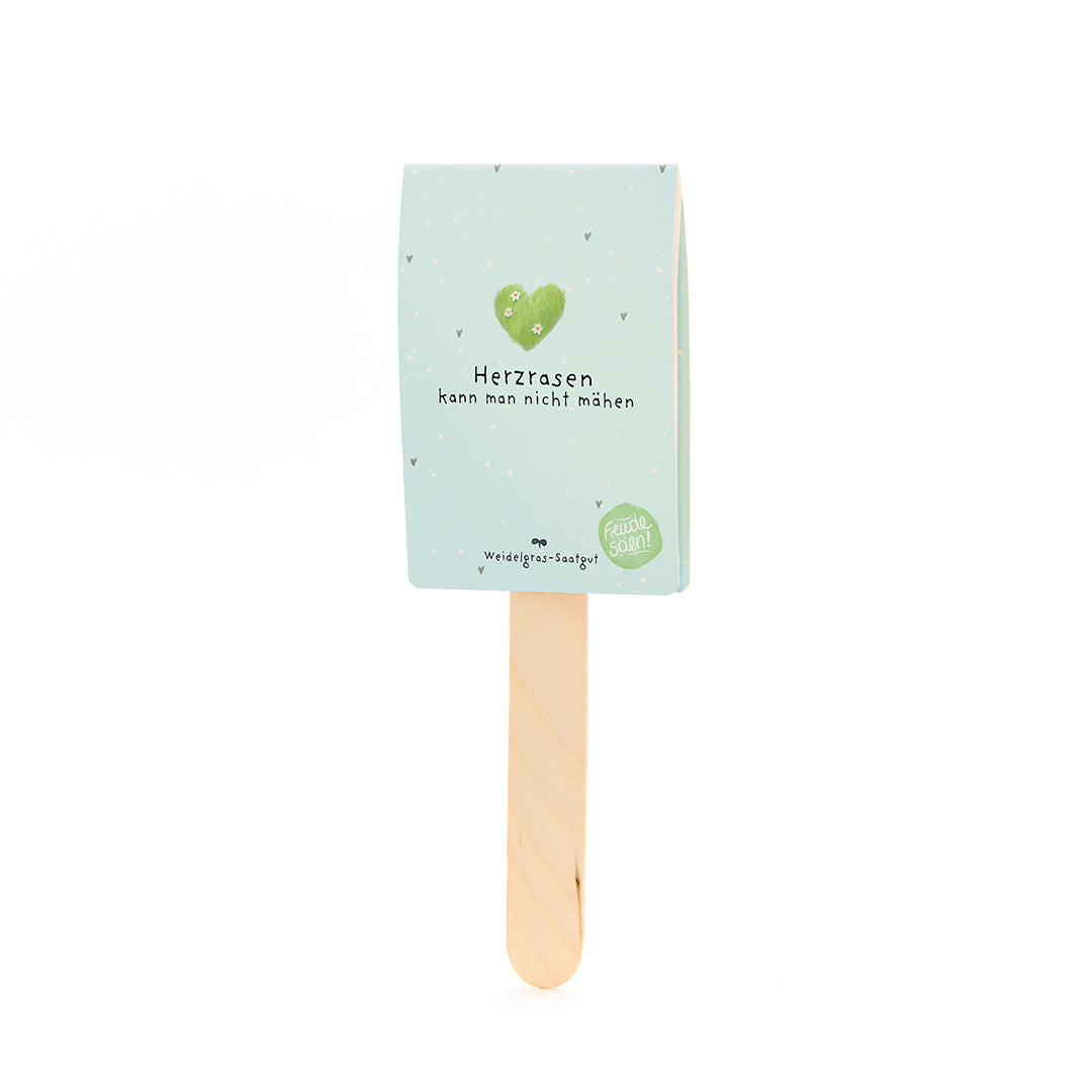 Bâton en bois avec un panneau bleu clair portant un cœur vert et le texte « On ne peut pas tondre un cœur qui court » et « Semences de gazon de pâturage ».
