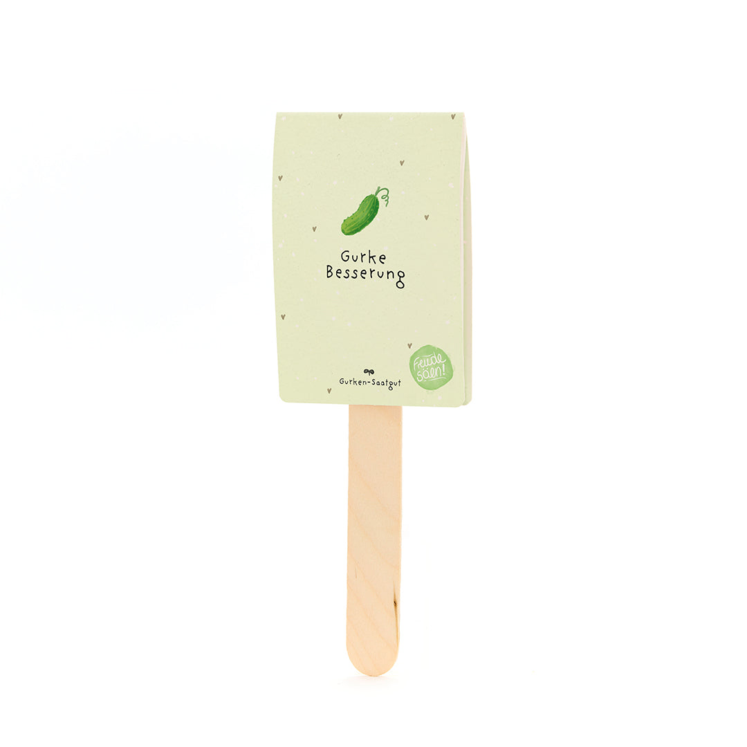 Un bâton en bois avec une étiquette en papier beige-vert représentant un concombre dessiné et le texte « Amélioration du concombre ».