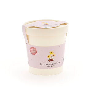 Pot de fleurs avec une étiquette rose sur laquelle est écrit « Fleur en chocolat pour toi » et présente un dessin d'une fleur sur un morceau de chocolat.