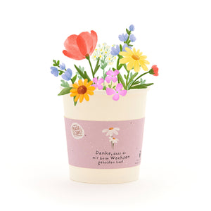 Un pot de fleurs avec des fleurs colorées et dessinées et un ruban sur lequel est écrit : « Merci de m'aider à grandir. »