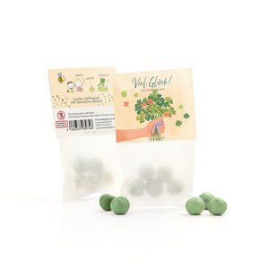 Sachet avec boules de graines vertes et graines de trèfle porte-bonheur, à côté de plusieurs boules vertes en vrac, sur l'emballage un motif de félicitations et une illustration de trèfle.