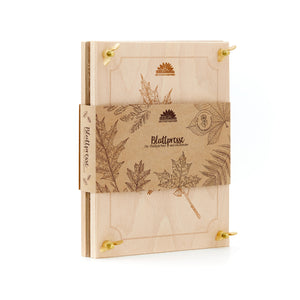 Presse à feuilles en bois avec gravures botaniques et bande de papier brun, sur laquelle sont imprimés des motifs de feuilles et l'inscription « Leaf Press ».
