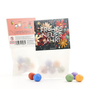 Deux sacs de boules de graines colorées, l'un avec un imprimé floral "Bonne année !" et l'autre avec des descriptions et des dessins, avec quelques boules posées devant.