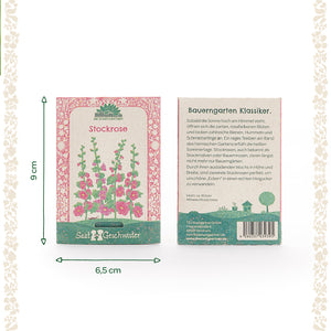 Deux sachets de graines de roses trémières de Saatgeschwister, l'un avec une illustration des fleurs et l'autre avec une description en allemand ; dimensions 9 cm de haut et 6,5 cm de large.