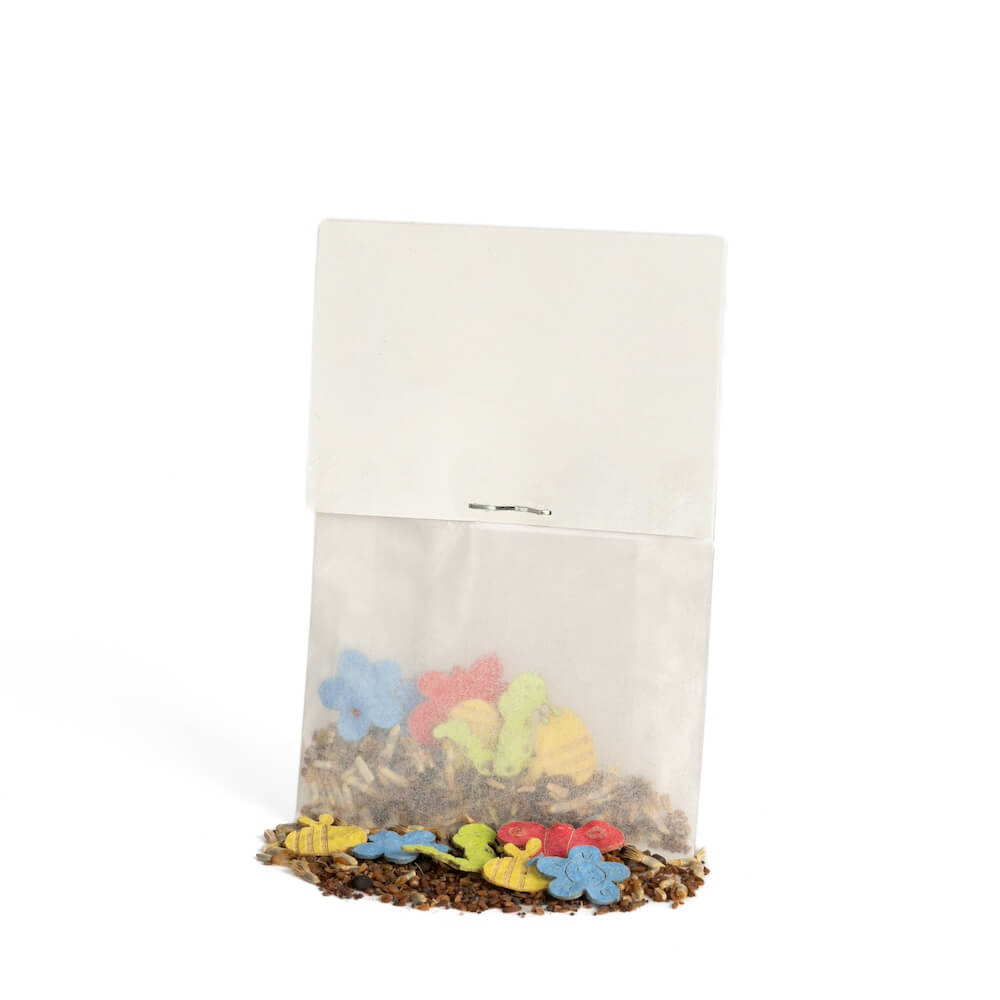 Petit sac en papier avec des biscuits colorés en forme de fleurs et d'animaux, dont certains sont tombés, sur un fond blanc.