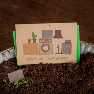 Carte de félicitations avec plantes en pot, machine à laver et lampe, texte : Tous mes vœux de bonheur dans votre nouvelle maison !
