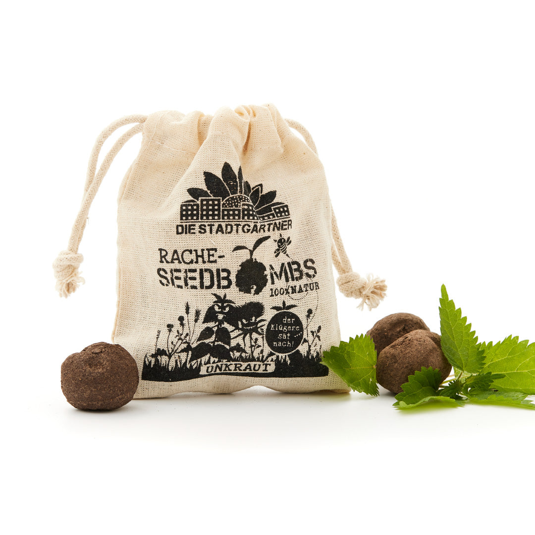"Un petit sac en jute avec l'imprimé 'THE CITY GARDENER'S REVENGE SEEDBOMBS 100% NATURAL' et quelques bombes à graines à côté de feuilles vertes fraîches sur fond blanc."
