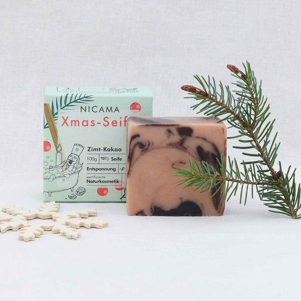 Savon artisanal au parfum de cannelle et de cacao à côté de son emballage et de sa décoration de Noël.