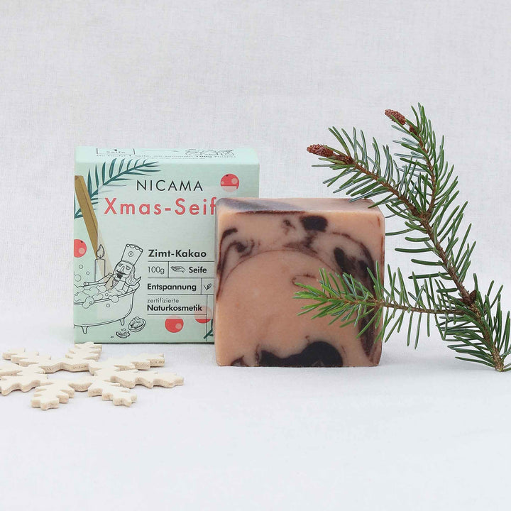Savon artisanal au parfum de cannelle et de cacao à côté de son emballage et de sa décoration de Noël.