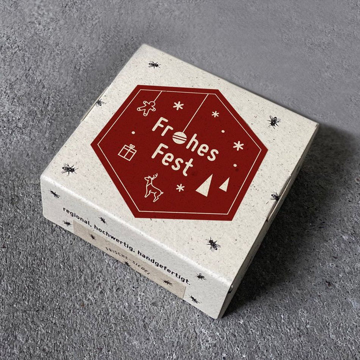 Coffret cadeau avec l'inscription "Joyeux Noël" et symboles de Noël sur fond gris.