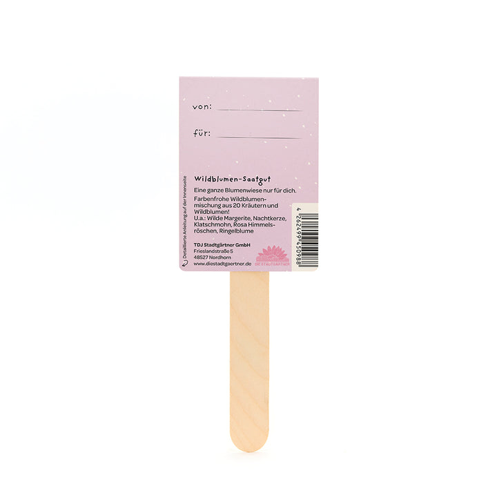 Dos d'un sachet de graines de fleurs sauvages avec un bâton en bois et une étiquette violette indiquant les champs « de » et « pour » et une description du mélange de fleurs sauvages.