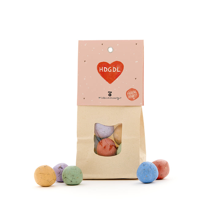 Sac en papier avec boules de graines colorées, étiquette avec un cœur rouge et l'inscription "H.D.G.D.L."