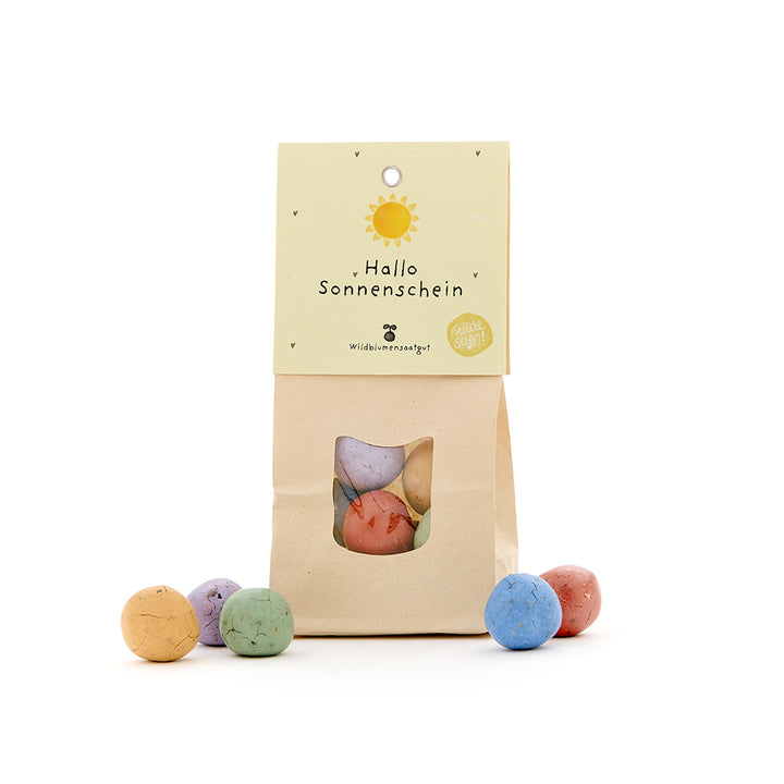 Sac en papier avec une fenêtre de visualisation, rempli de boules de graines colorées, étiquette avec l'inscription « Hello Sunshine ».