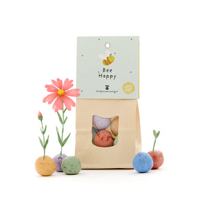 Sac en papier avec l'inscription "Bee Happy" et des bombes de graines colorées faisant pousser des fleurs.