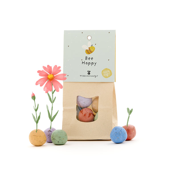 Sac en papier avec l'inscription "Bee Happy" et des bombes de graines colorées faisant pousser des fleurs.