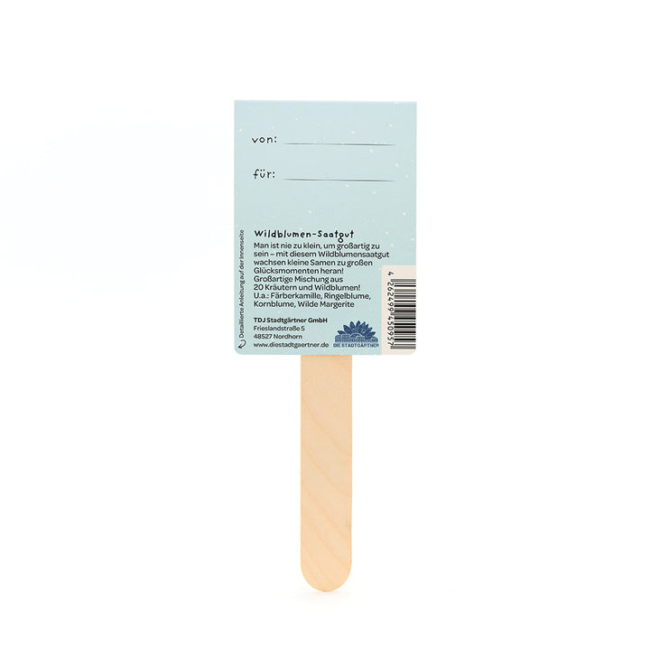 Dos d'un bâtonnet de graines de fleurs sauvages avec un texte descriptif, un espace pour les entrées « de » et « pour », ainsi que des informations sur le produit et le fabricant sur un fond bleu clair.