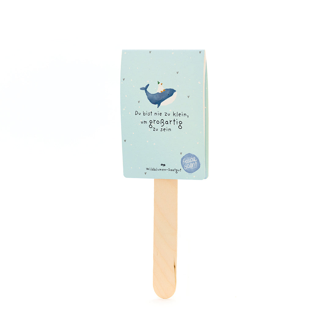 Bâtons en bois avec une étiquette en papier bleu clair représentant une baleine avec un chapeau de fête et le texte « Vous n'êtes jamais trop petit pour être grand ».