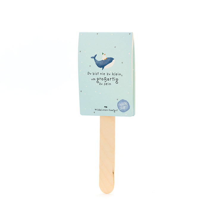Bâtons en bois avec une étiquette en papier bleu clair représentant une baleine avec un chapeau de fête et le texte « Vous n'êtes jamais trop petit pour être grand ».