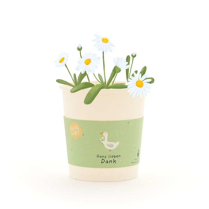 Un pot de fleurs de couleur crème avec des marguerites blanches et une étiquette verte, comportant un dessin d'une oie et le texte « Merci beaucoup, Oie ».
