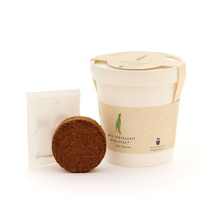 Un kit de plantation avec un bloc de terre rond, un sac de graines et un récipient beige.