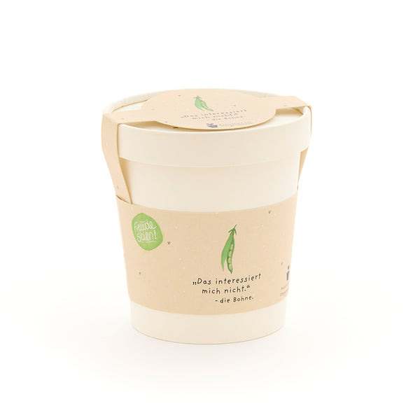 Une tasse blanche avec une étiquette beige représentant un petit pois vert et la phrase « Je m'en fiche. – le haricot. »