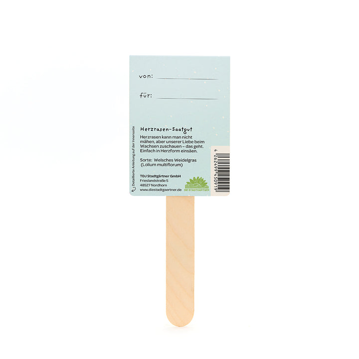 Bâton en bois avec une carte bleu clair attachée, avec des champs de texte « de » et « pour » ainsi que des informations sur les graines de palpitations cardiaques en allemand.