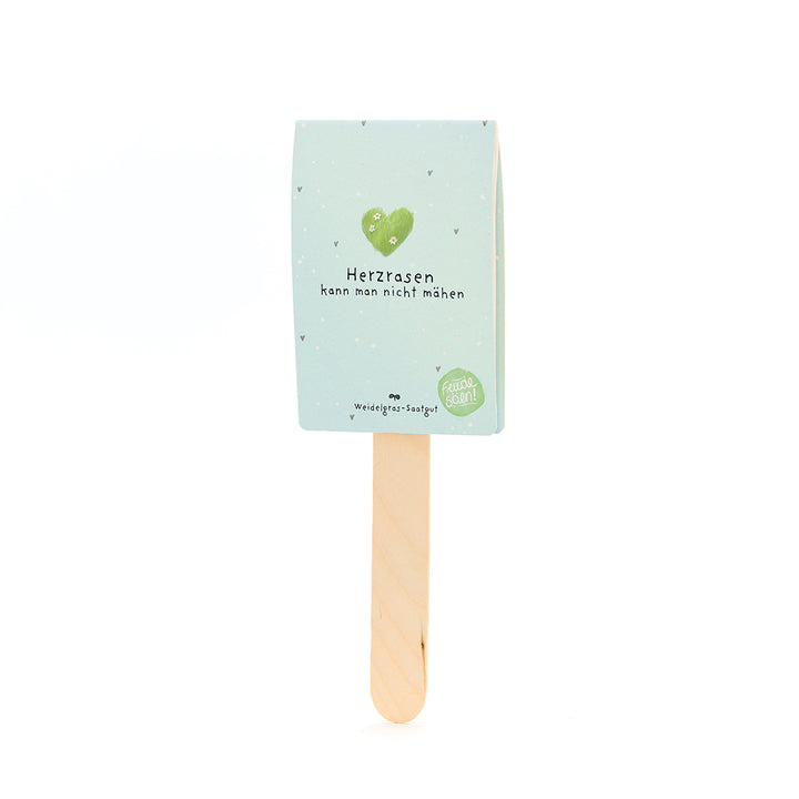 Bâton en bois avec un panneau bleu clair portant un cœur vert et le texte « On ne peut pas tondre un cœur qui court » et « Semences de gazon de pâturage ».