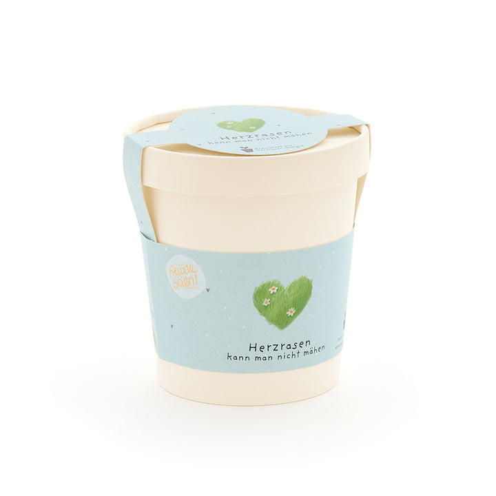 Pot de fleurs beige avec une étiquette bleu clair, un cœur vert et l’inscription « On ne peut pas tondre un cœur qui court ».