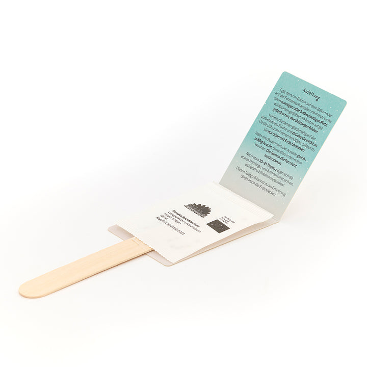 Un ensemble composé d'un bâton en bois, d'un sachet de graines et d'une carte d'instructions dépliée sur fond blanc.