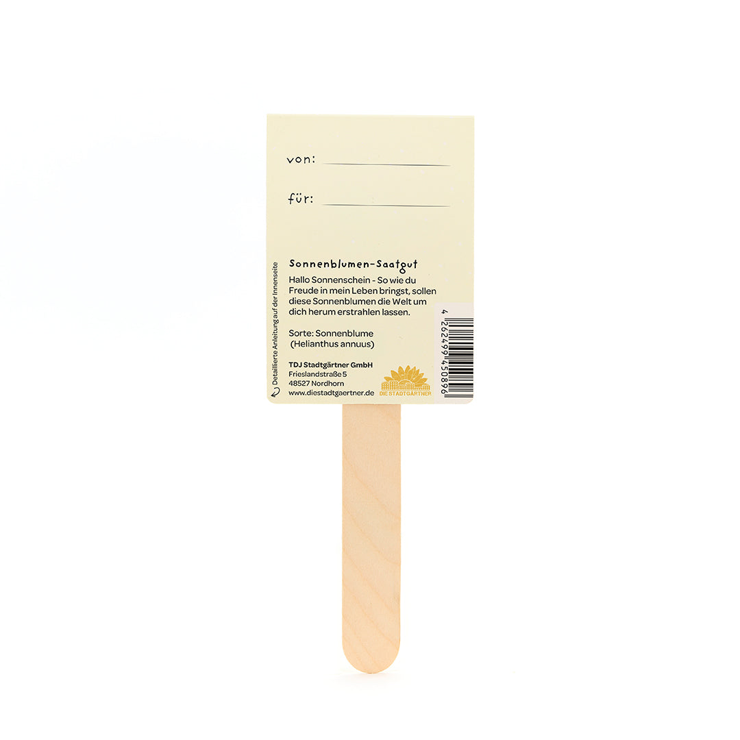 Un bâton en bois avec une étiquette attachée décrivant les graines de tournesol et contenant des cases « de » et « pour » à remplir.