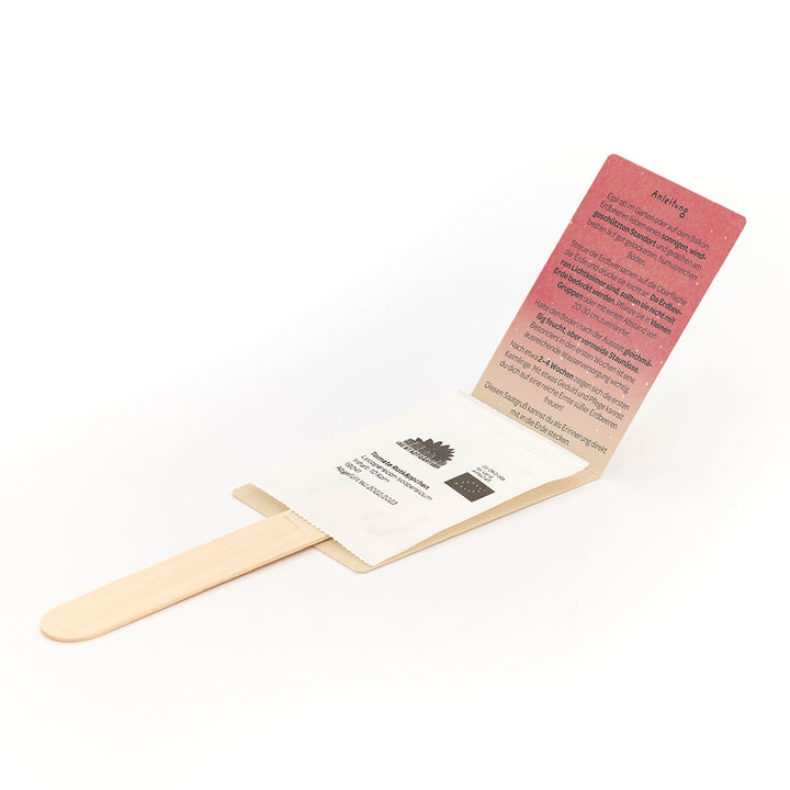 Un kit de graines en forme de tige en bois avec emballage en papier déplié et instructions en allemand.