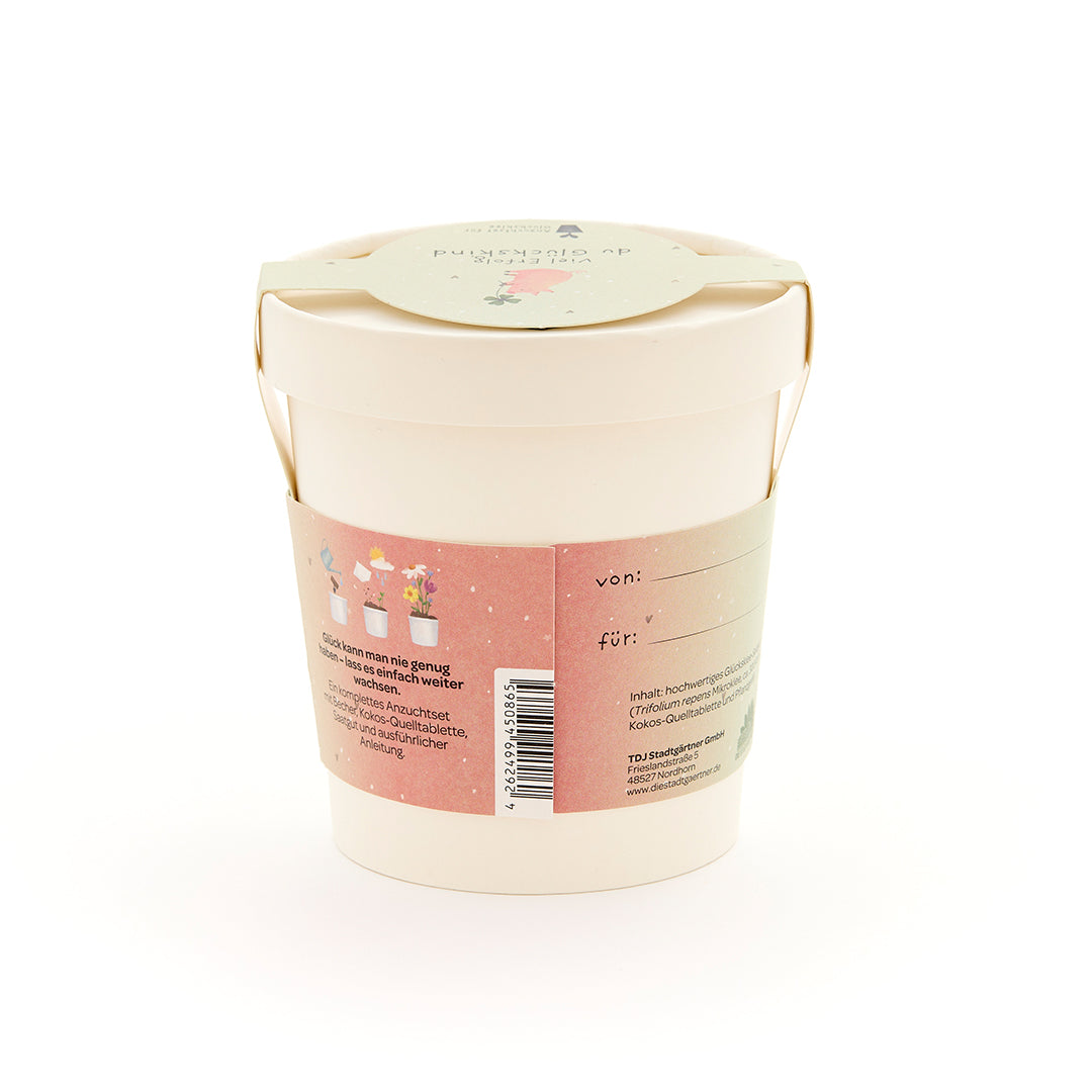 Pot de fleurs beige avec une étiquette rose comportant des illustrations florales et un champ « de : » et « pour : », ainsi qu'un texte supplémentaire.