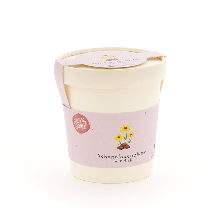 Pot de fleurs avec une étiquette rose sur laquelle est écrit « Fleur en chocolat pour toi » et présente un dessin d'une fleur sur un morceau de chocolat.