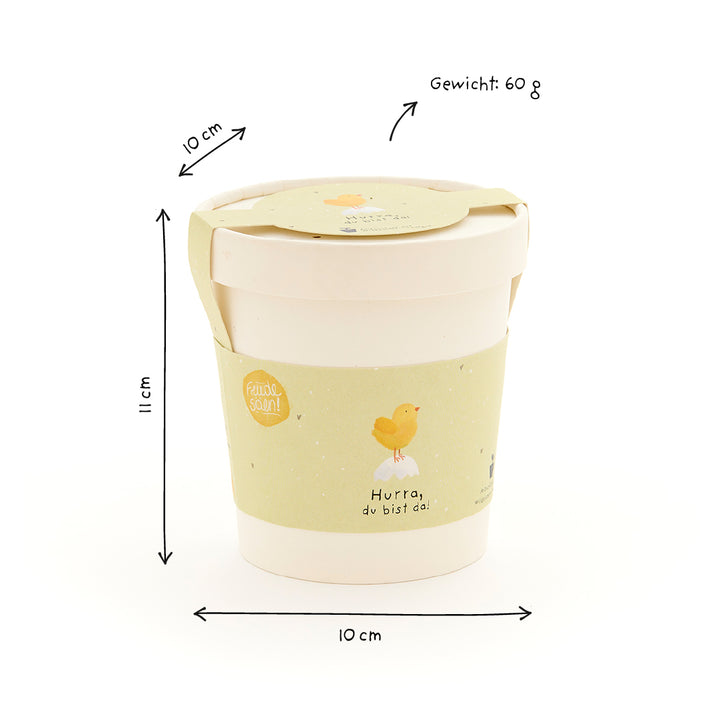 Mug beige avec étiquette jaune, illustration de poussin et texte "Hourra, tu es là !", avec dimensions (10 cm de diamètre, 11 cm de hauteur) et poids (60 g) en allemand.