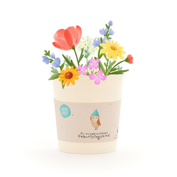 Un pot de fleurs avec des fleurs colorées et un ruban avec l’inscription « Toi, magnifique enfant fêté ».