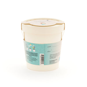 Pot de fleurs beige avec étiquette et anse bleues, coffret cadeau pour une prairie fleurie, étiquettes "de" et "pour" visibles.