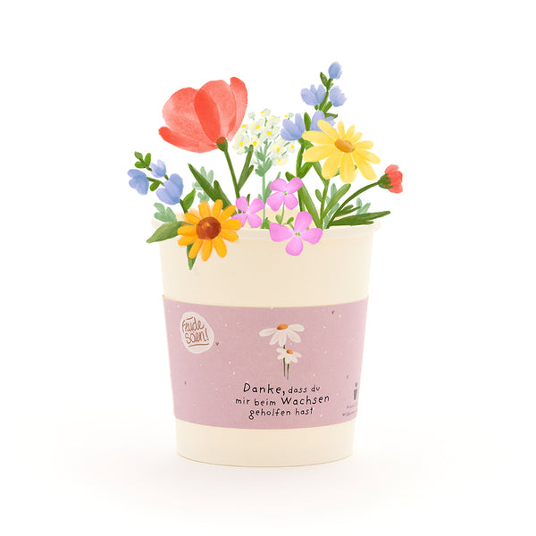 Un pot de fleurs avec des fleurs colorées et dessinées et un ruban sur lequel est écrit : « Merci de m'aider à grandir. »