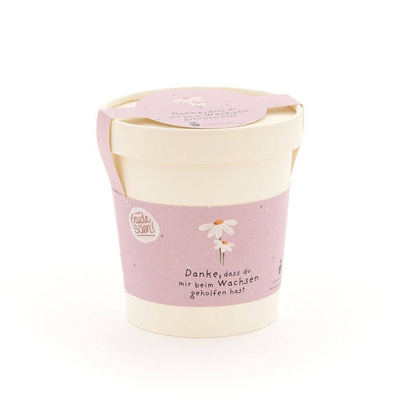 Pot de fleurs beige avec un ruban rose, une fleur dessinée et le texte « Merci de m'aider à grandir ».