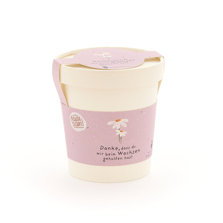 Pot de fleurs beige avec un ruban rose, une fleur dessinée et le texte « Merci de m'aider à grandir ».