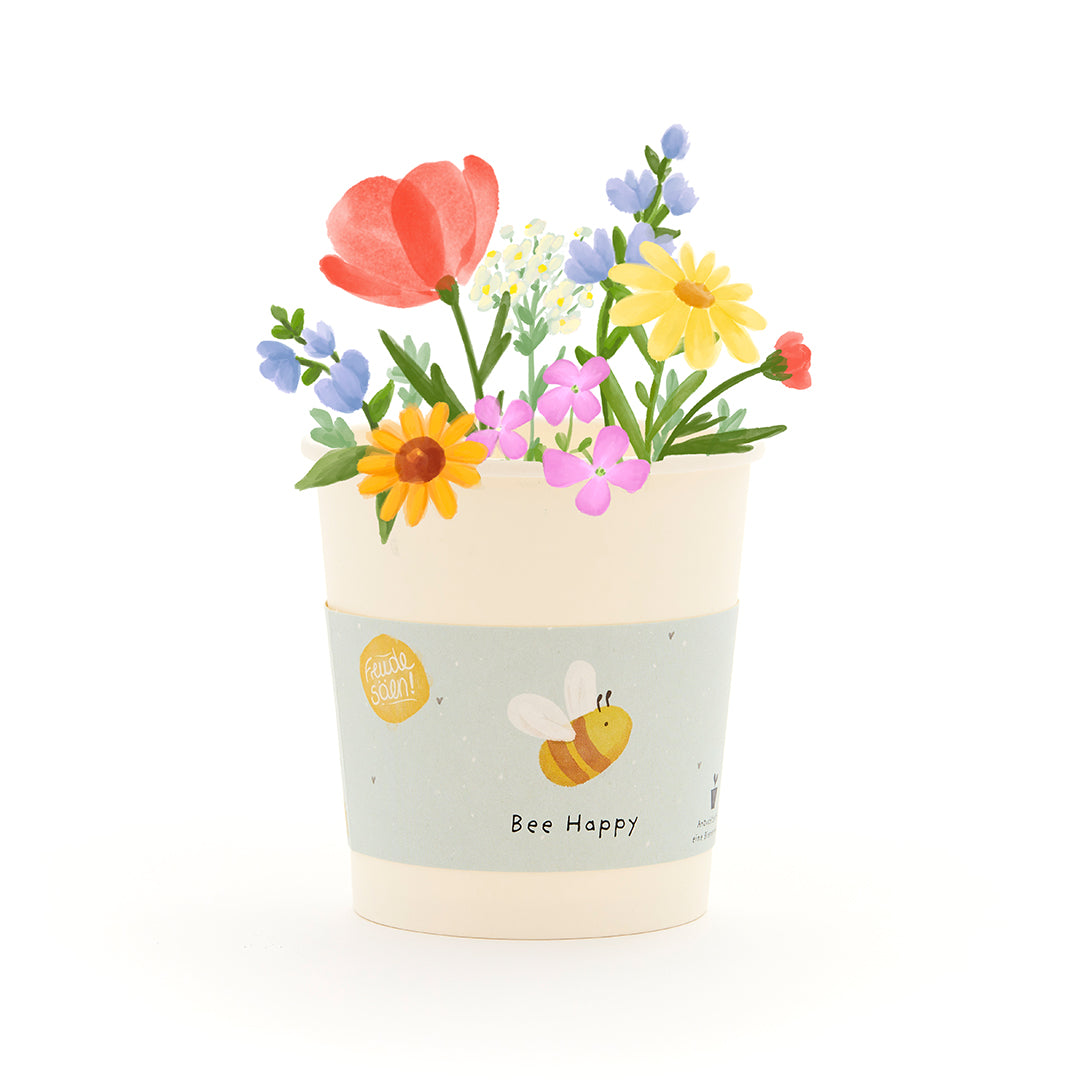 Pot de fleurs avec des fleurs colorées et une abeille sur l'étiquette qui dit "Bee Happy".
