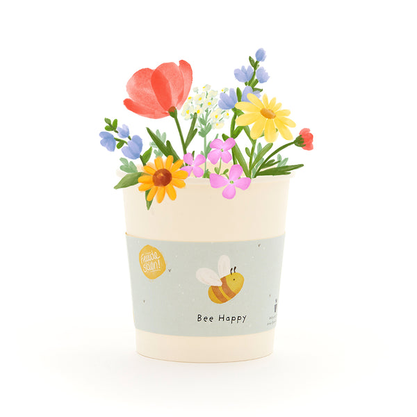 Pot de fleurs avec des fleurs colorées et une abeille sur l'étiquette qui dit "Bee Happy".