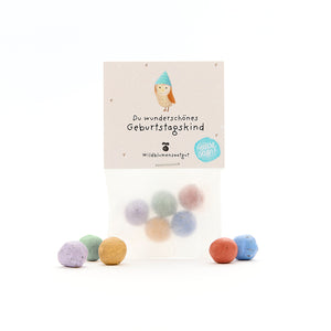 Un sachet de boules de graines de fleurs sauvages colorées et une carte d’anniversaire avec l’inscription « Toi, magnifique enfant fêté ».