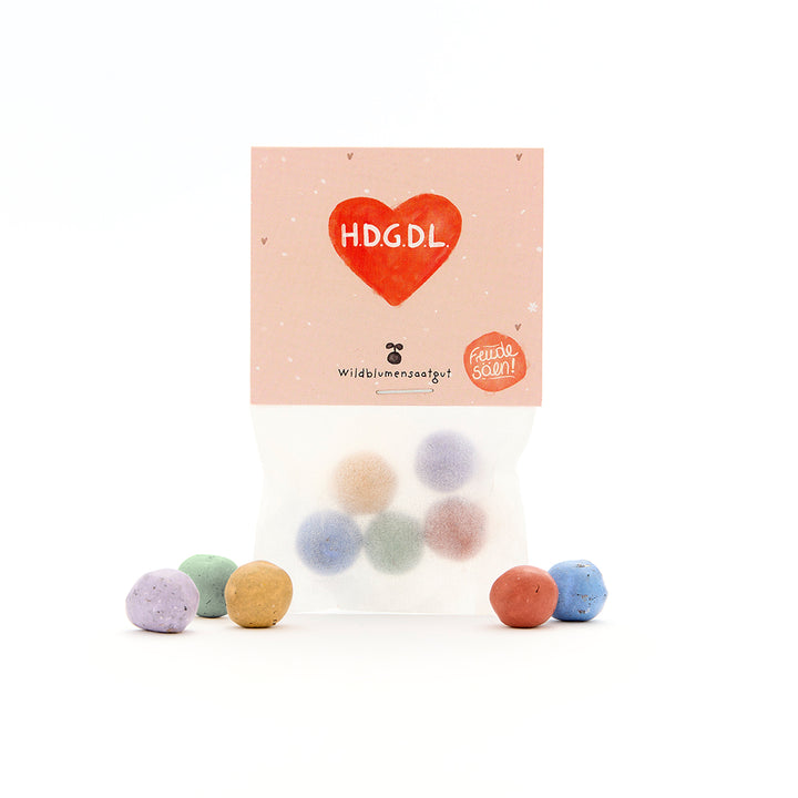 Sachet de boules de graines colorées, l'emballage indique « H.D.G.D.L » dans un cœur rouge et « graines de fleurs sauvages ».