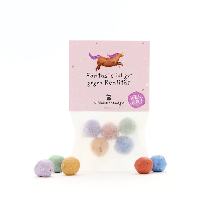 Sachet contenant des boules de graines colorées et un emballage violet avec une licorne et le texte « L’imagination est bonne contre la réalité ».