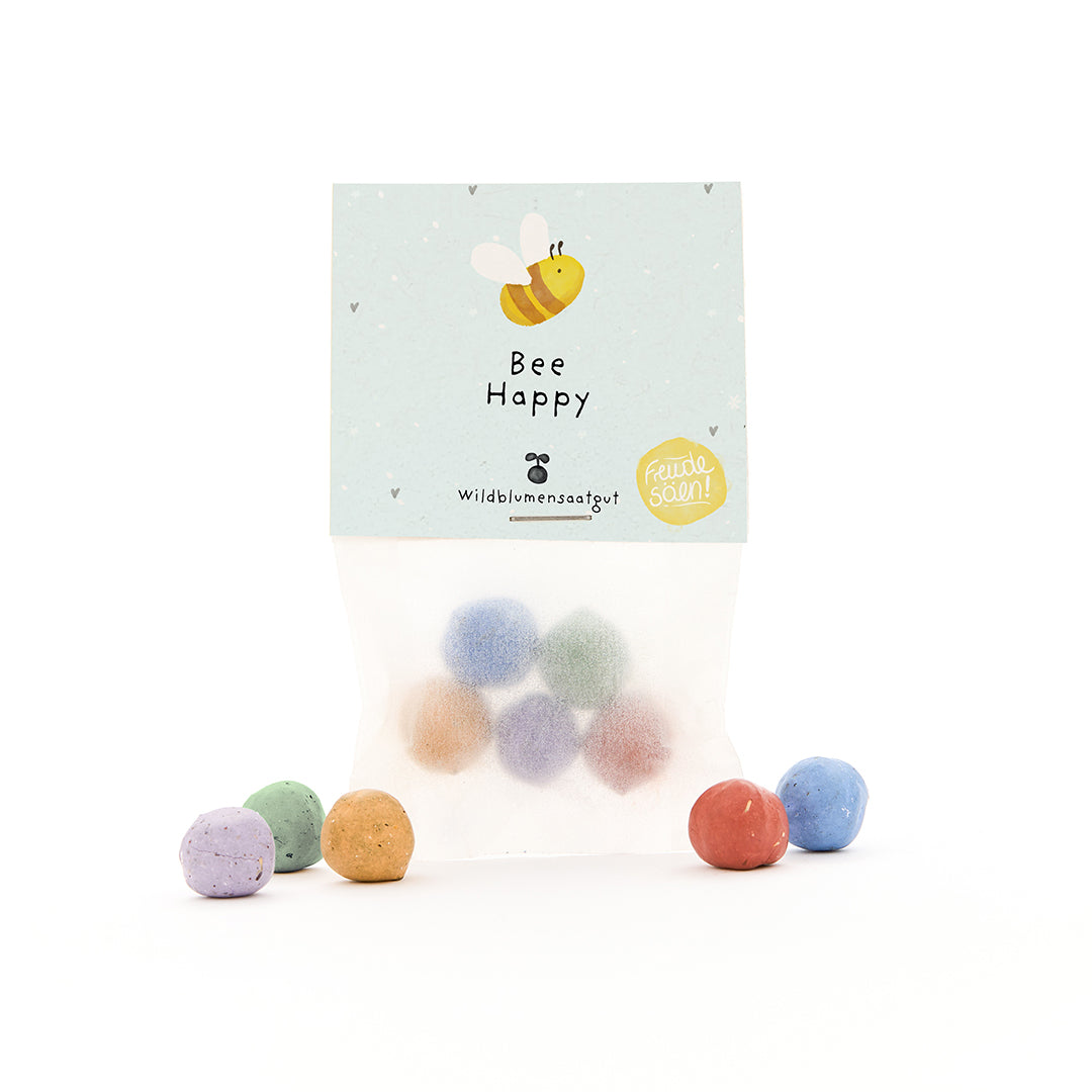 Sac avec des bombes de graines colorées et une étiquette "Bee Happy" et une abeille dessinée.