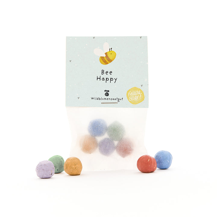 Sac avec des bombes de graines colorées et une étiquette "Bee Happy" et une abeille dessinée.