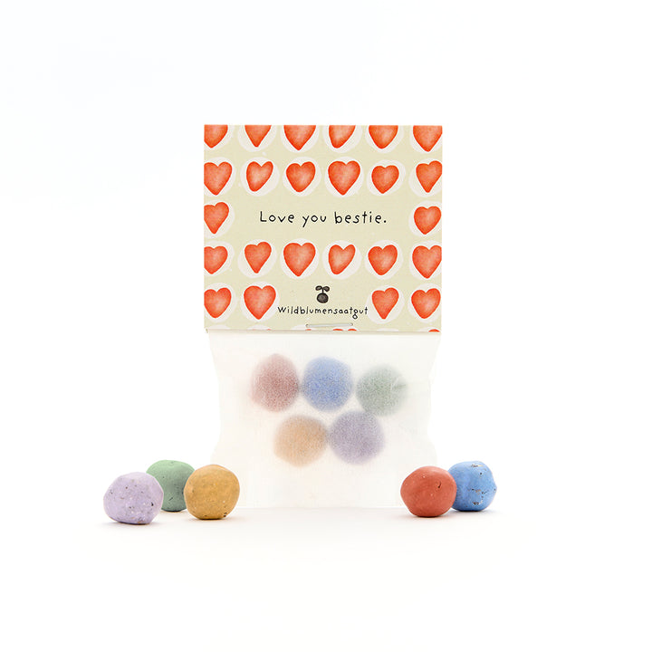 Un sac de boules de graines colorées, avec une carte avec des cœurs rouges et le texte « Je t'aime ma meilleure amie. Graines de fleurs sauvages. »