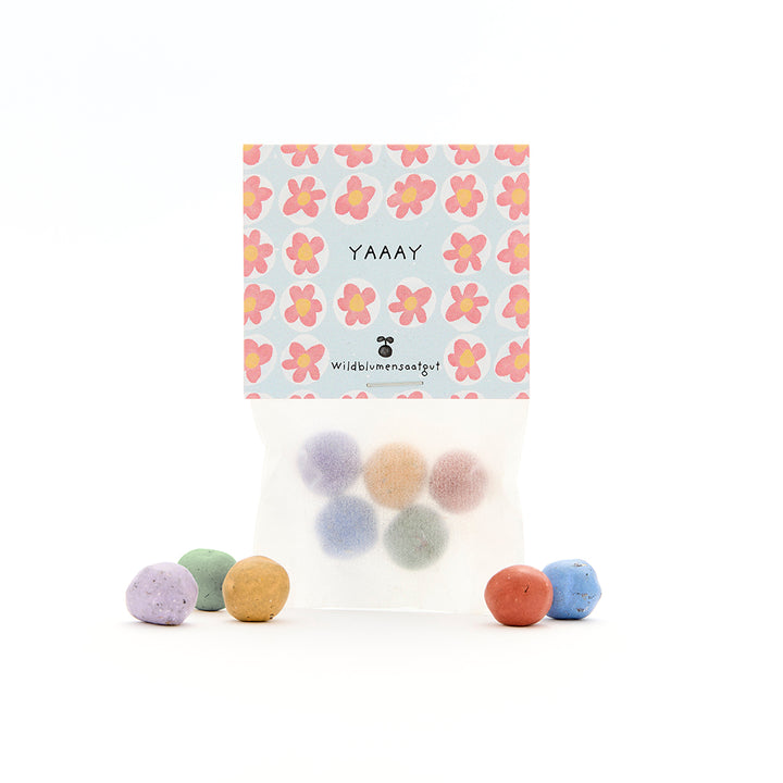 Boules de graines multicolores dans un emballage transparent avec une étiquette florale et l'inscription "YAAAY".