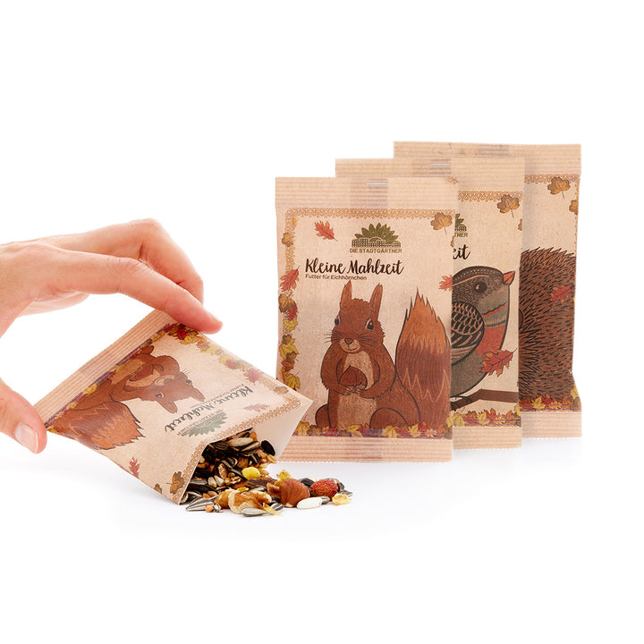 « Une main ouvre un petit sac en papier contenant de la nourriture pour animaux, à côté de deux autres sacs avec des illustrations d'écureuil et de hérisson »