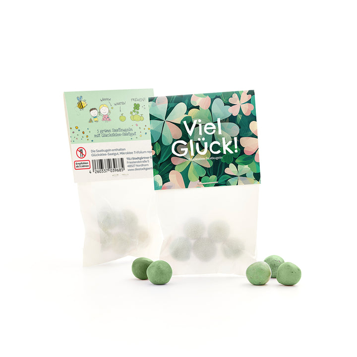 Deux petits sachets de boules de graines vertes, l'un avec un motif de trèfle et les mots "Bonne chance !", l'autre avec le dos et la description et les dessins.